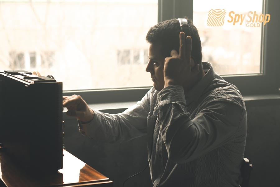 Mężczyzna obsługuje specjalistyczny sprzęt do podsłuchu, ma założone słuchawki i trzyma je ręką.